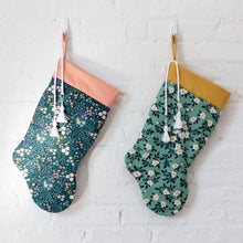 Load image into Gallery viewer, Two stockings made in floral fabrics, hung against a white brick wall
