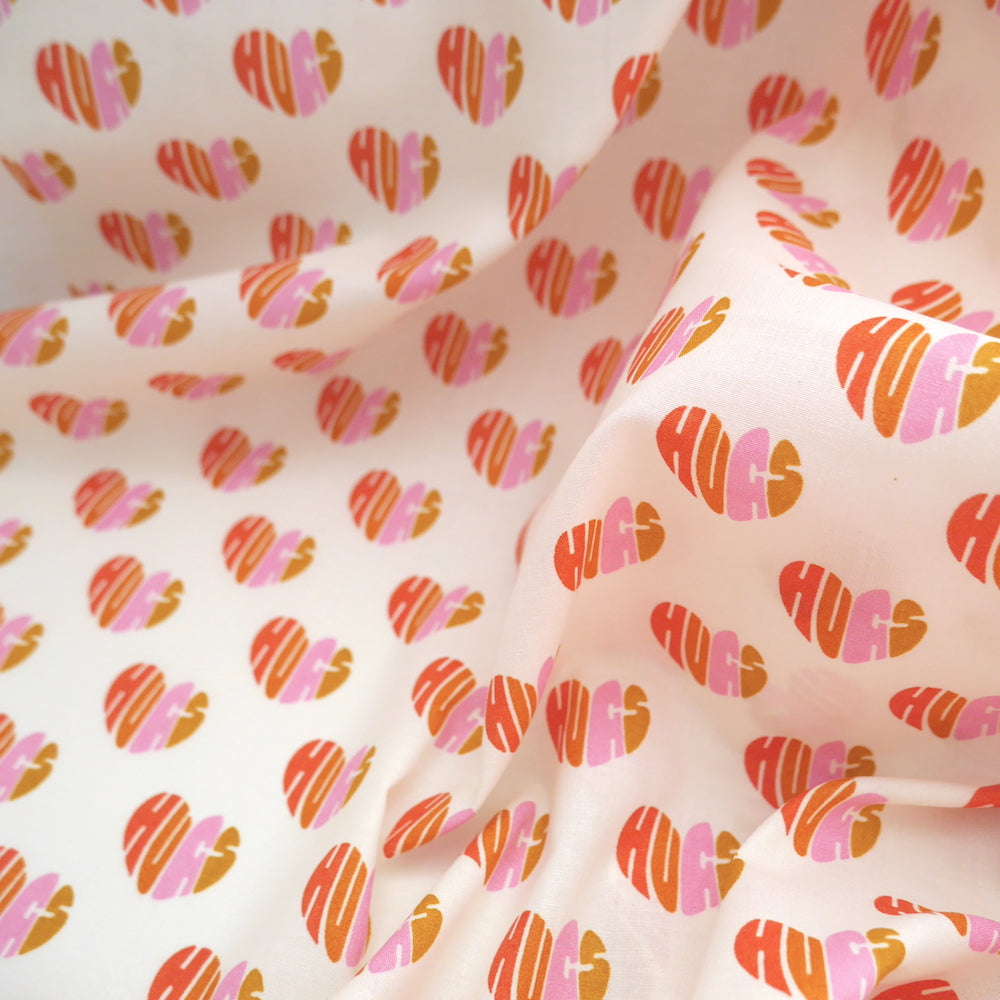 Organic Cotton Fabric slightly crumpled shows pattern of loveheart shaped 'hugs' words