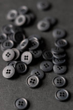 Load image into Gallery viewer, Collection of Scuttle Black Cotton buttons with four holes piled on surface.
