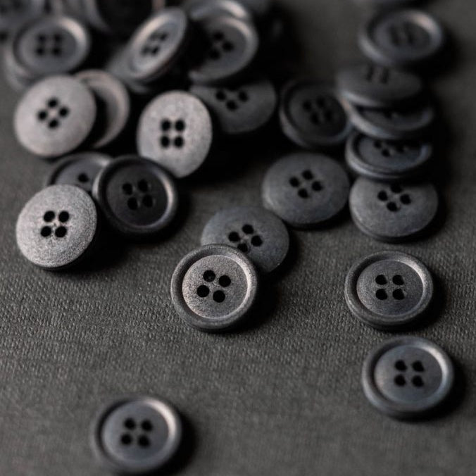 Collection of Scuttle Black Cotton buttons with four holes piled on surface.