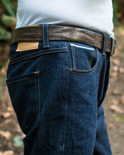 Load image into Gallery viewer, Close up side view at hip level of denim blue jeans. Shows flat-fell seams in contrasting yellow top stitching and rivets of front pocket corners.
