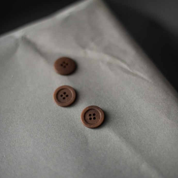 Three buttons spread out on a piece of paper which a rim and four sewing holes