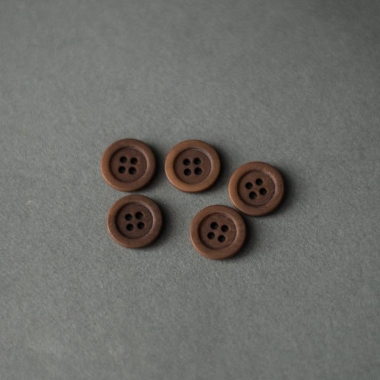 Five buttons laid on paper, classic button with rim and 4 sewing holes. Looks very similar to a wood material.