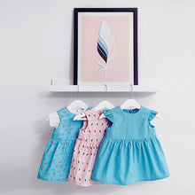 Load image into Gallery viewer, Three hanging babywear dresses made with Lightening Lily Crystal Blue Cotton Fabric, and other fabrics from the Soft Cactus collection.
