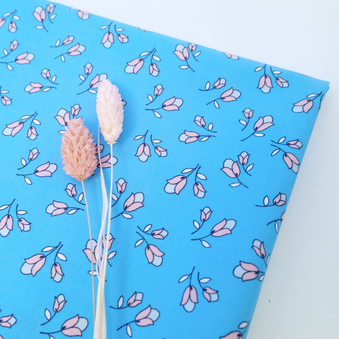Two tone pink tulip prints on blue background. Folded fabric, displayed with two pink dried flowers stems.