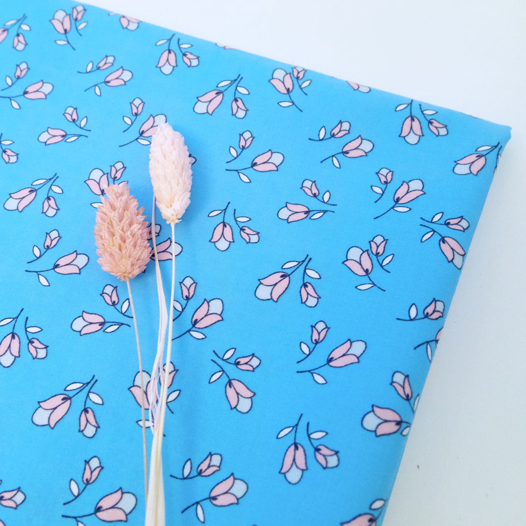 Two tone pink tulip prints on blue background. Folded fabric, displayed with two pink dried flowers stems.