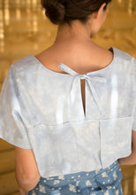 Load image into Gallery viewer, Back view of lady wearing a short sleeve top with inverted box pleat into a yoke, open at centre-back, fastened with knotted ties
