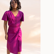 Load image into Gallery viewer, Lady wears a V-neck button front blouse, with pleated shoulder seams and short sleeves, with a wrap skirt.
