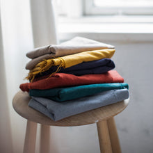 Load image into Gallery viewer, Pile of folded fabrics on a stool shows Stretchy Spot jacquard in six different colours.
