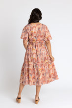 Load image into Gallery viewer, Back view of lady wearing Protea dress with one hand in pocket, one holding out tiered skirt
