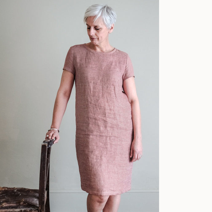 Lady stands by a chair wearing a Camber Set Dress, t-shirt dress, knee length