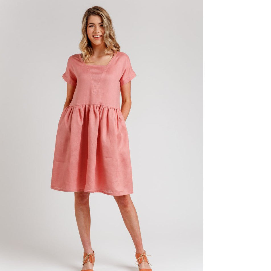 Lady stands with hands in pockets in a V-neck insert bodice with gathered waist knee length dress