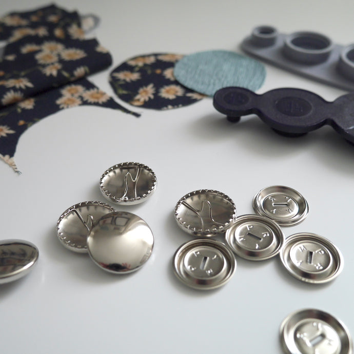 23mm metal cover button blanks displayed next to cover tool and circular pieces of fabric