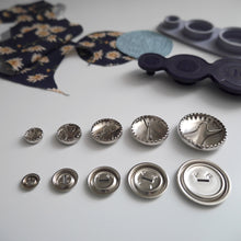 Load image into Gallery viewer, 5 different sized metal cover button blanks underneath displayed next to cover tool and circular pieces of fabric
