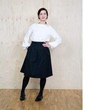Load image into Gallery viewer, Lady stands wearing a white top with wide neckline and long sleeves which puff at the wrist. Worn with the Three Pleat Skirt.
