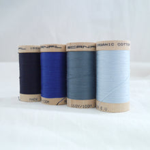 Load image into Gallery viewer, Four wooden reels of organic cotton sewing thread, navy, bright royal blue, dusty blue, pale blue.
