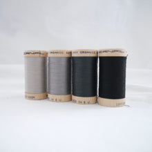 Load image into Gallery viewer, Four wooden reels of organic cotton sewing thread in Sand, Steel Grey, Charcoal and Black Onyx colours
