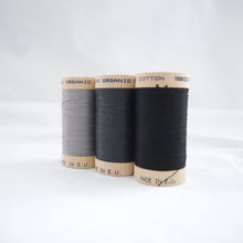 Load image into Gallery viewer, Three wooden reels of organic cotton sewing thread in Steel Grey, Charcoal and Black Onyx colours
