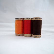 Load image into Gallery viewer, Wooden reels of organic cotton sewing thread in Tangerine, Ruby Red and Mid Brown colours
