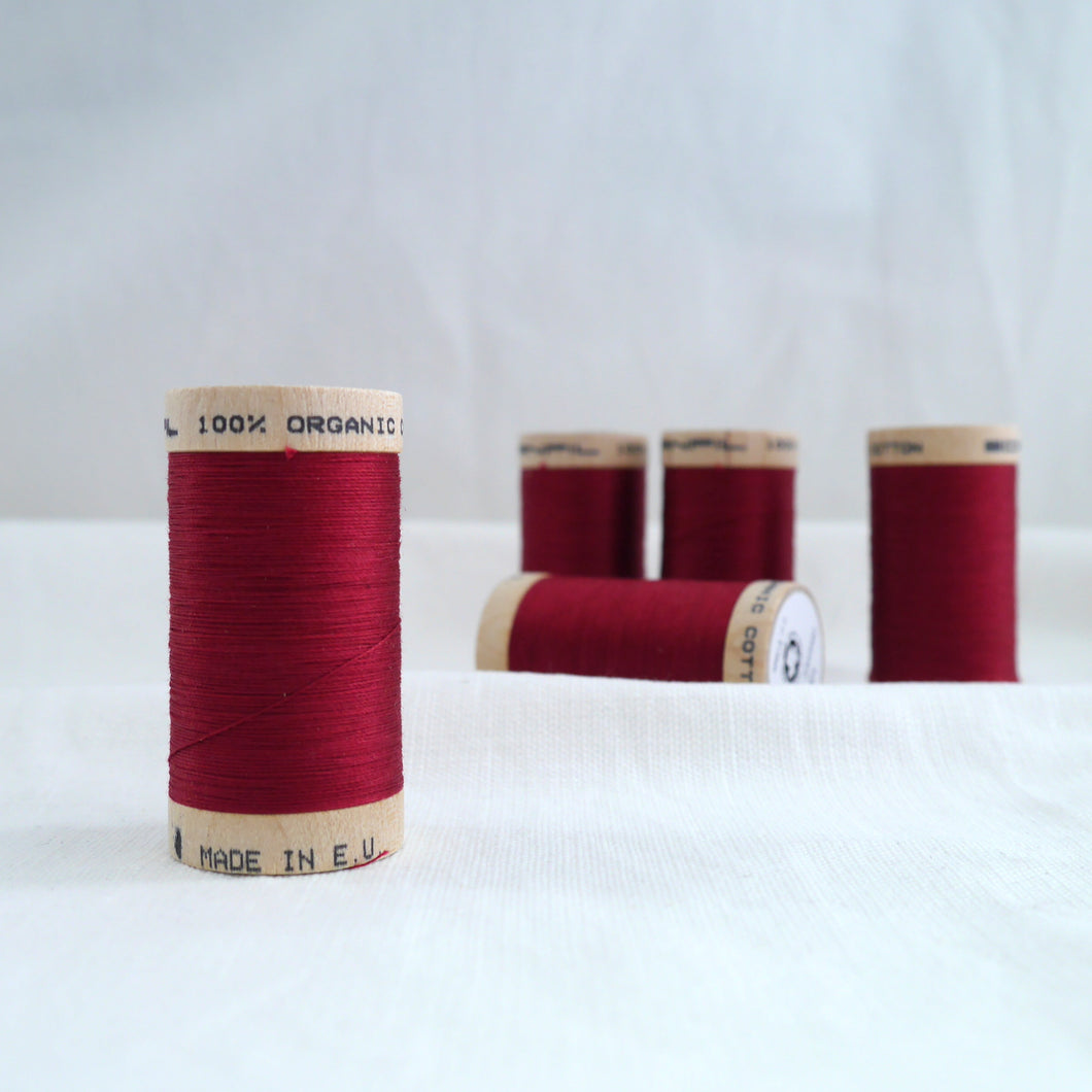 Collection of five wooden reels of organic cotton sewing thread in a dark red colour.