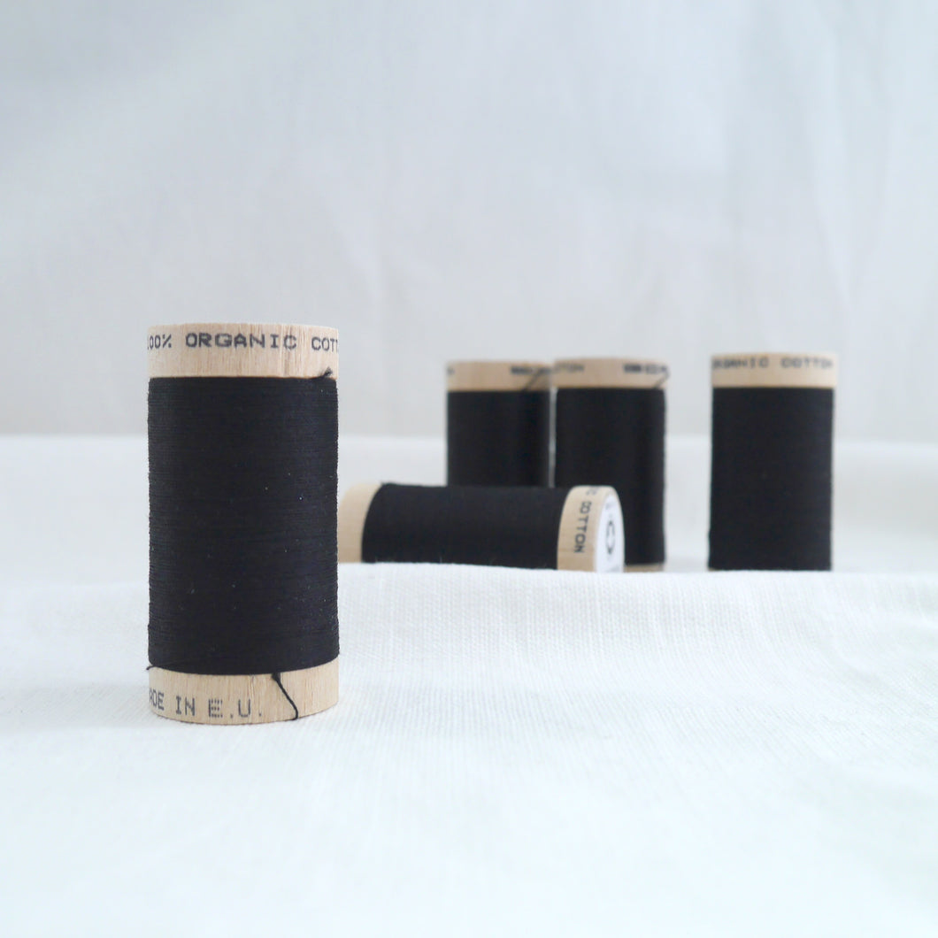 Five wooden reels of organic cotton sewing thread in black.