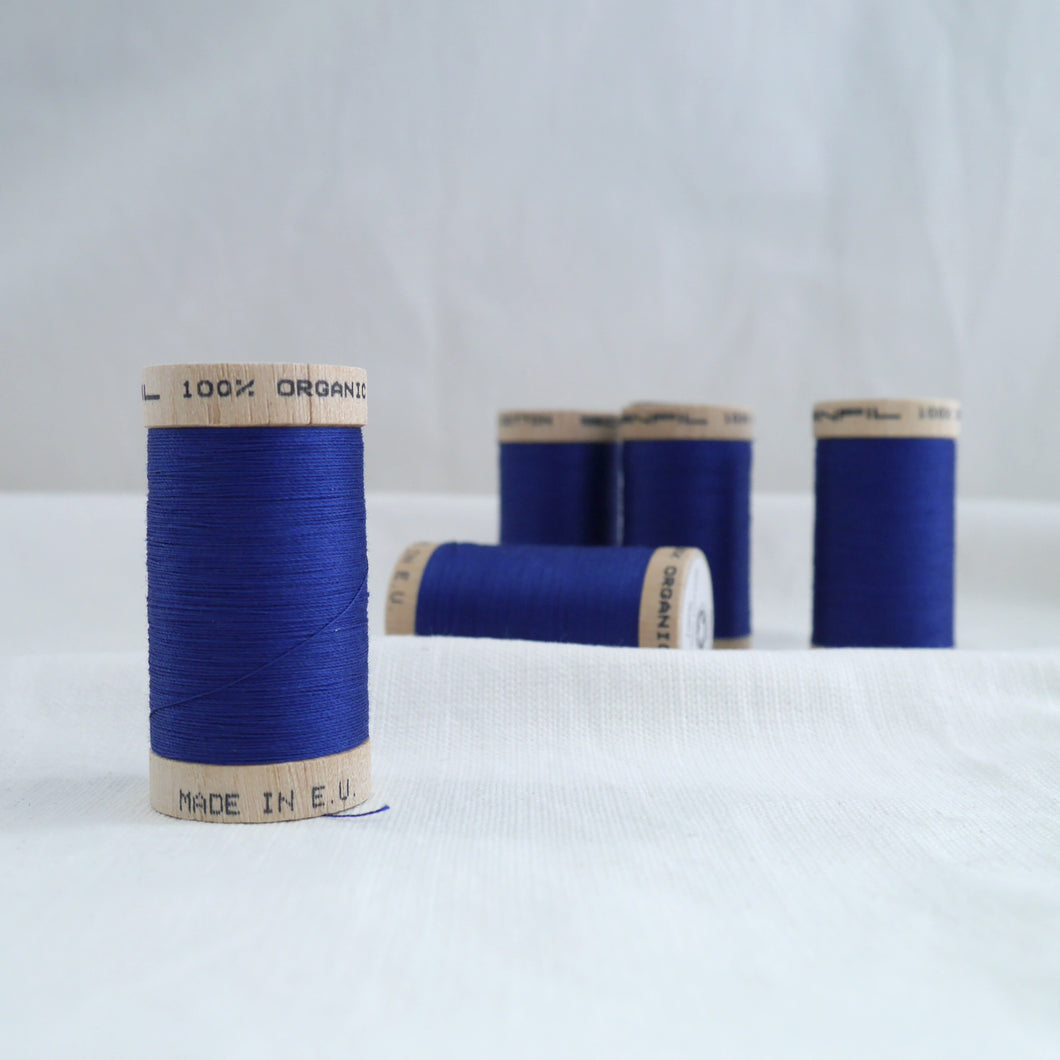 Five wooden reels of organic cotton sewing thread in a royal blue ocean.