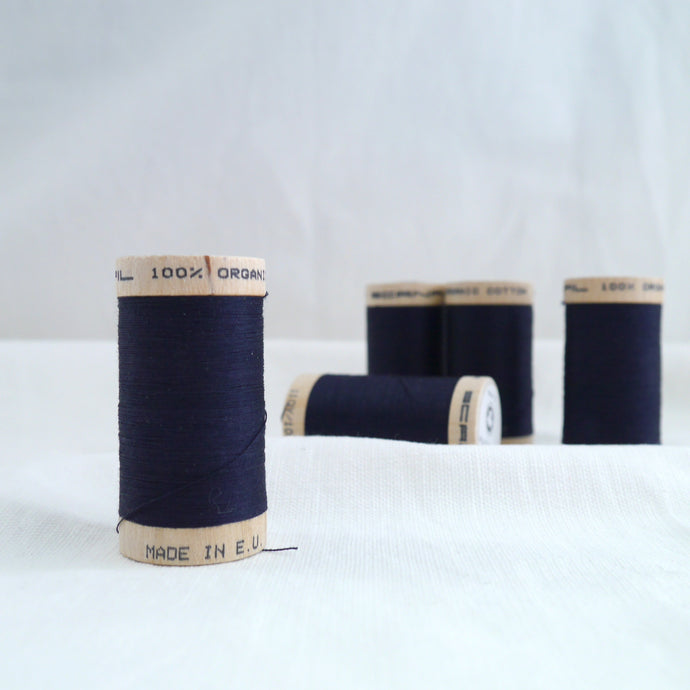 Five wooden reels of organic cotton sewing thread in a dark navy midnight blue.