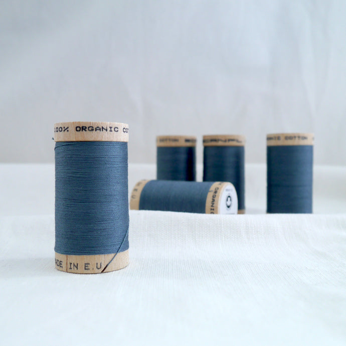 Five wooden reels of organic cotton sewing thread in a dusty Stormy blue colour.