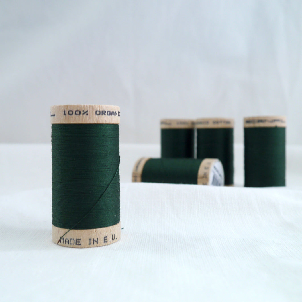 Five wooden reels of organic cotton sewing thread in a forest green colour.
