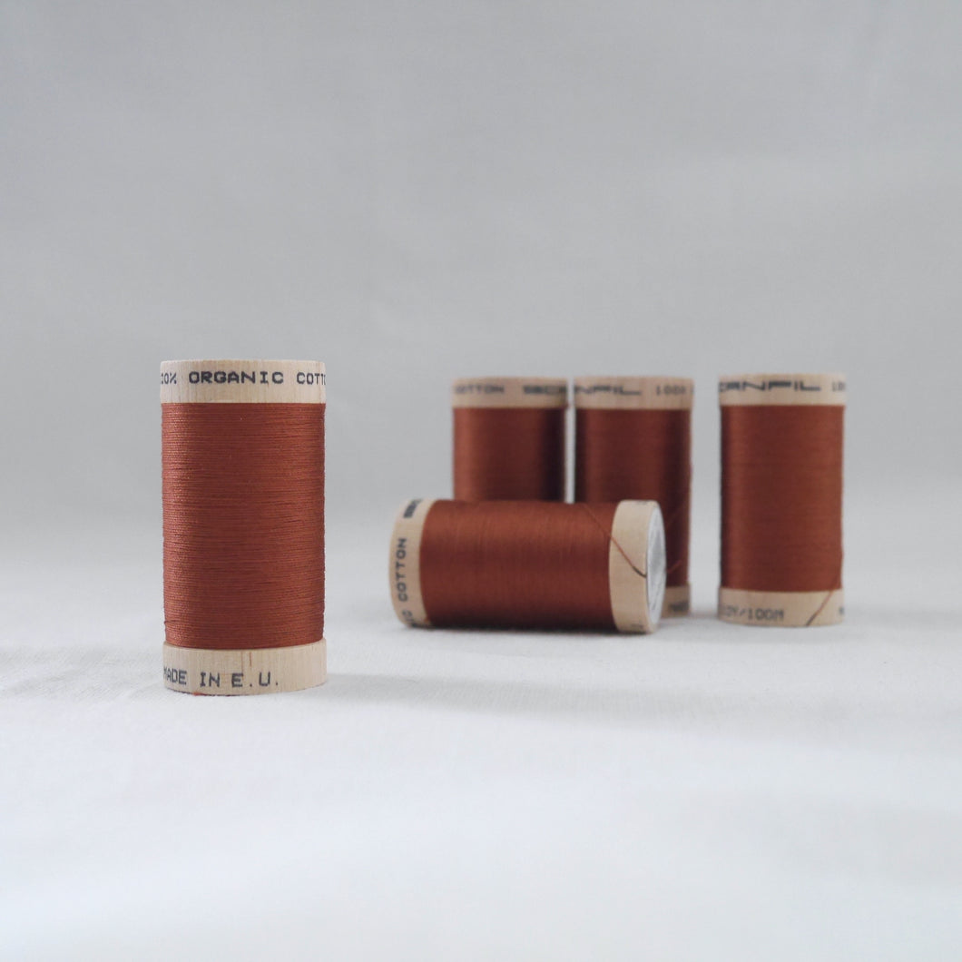 Five wooden reels of organic cotton sewing thread in a copper colour