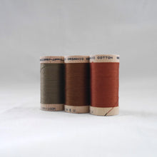 Load image into Gallery viewer, Three wooden reels of organic sewing cotton threads in khaki, acorn brown, and copper colours.

