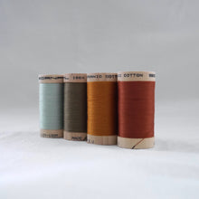 Load image into Gallery viewer, Line of four wooden reels of organic cotton sewing thread in mint, khaki, gold ochre, and copper colours.
