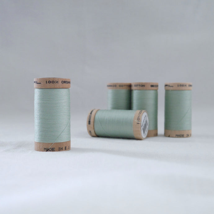 Four wooden reels of organic cotton sewing threads in a light mint green colour