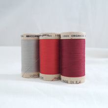 Load image into Gallery viewer, Three wooden spools of organic cotton sewing thread in silver, ruby red, and wine red colours.
