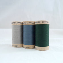 Load image into Gallery viewer, Three wooden spools of organic cotton sewing thread. Silver grey, stormy blue and forest green.
