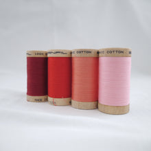 Load image into Gallery viewer, Four wooden reels of Scanfil Organic Cotton Thread in Wine, Ruby Red, Salmon and Carnation Pink colours.
