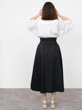 Load image into Gallery viewer, Back view of lady wearing the V-Neck Cuff Top tucked into a skirt, round neckline
