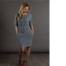 Load image into Gallery viewer, Lady stands wearing an elbow-length sleeve dress, with hands in pockets. Dress just above knee-length. Made in a diamond pattern print fabric.
