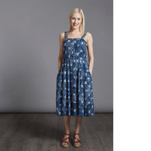 Load image into Gallery viewer, Lady stands wearing strap top with four buttons down centre front, pleated in skirt at waistline, dress length below the knee. Dress in a blue and white round pattern fabric. Lady has hands in pockets.
