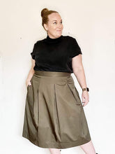 Load image into Gallery viewer, Lady wears three pleat skirt in a shiny gold green fabric. Worn with plain black velvet tee.

