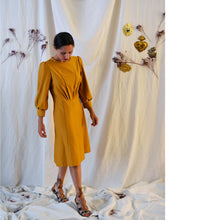 Load image into Gallery viewer, Lady wears a yellow Zenith dress with puff sleeves, and pleating details that sunrays from the waistline. Skirt length below the knee.
